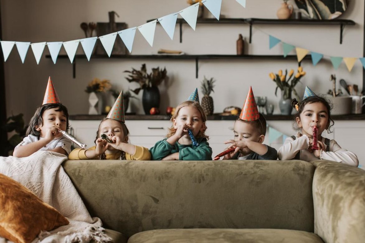 Five happy kids in party hats blowing party horns at a birthday party